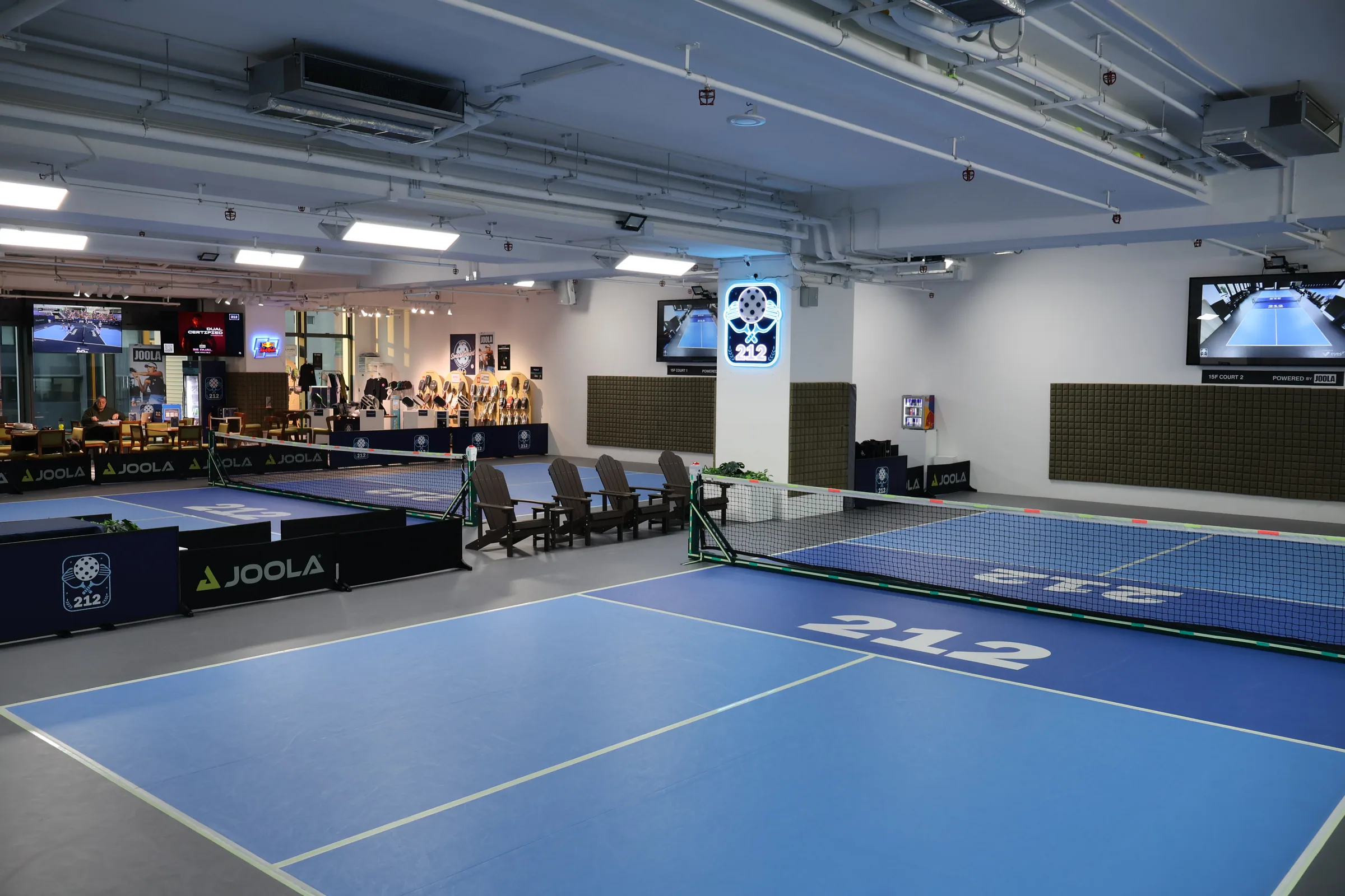 Two of 212HK's permanent indoor courts with the neon 212 sign and café behind